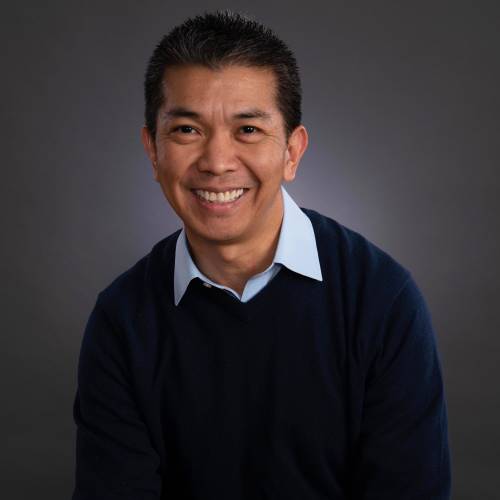 Dr. Vasquez is smiling in a dark blue sweater and a light blue collared shirt. 